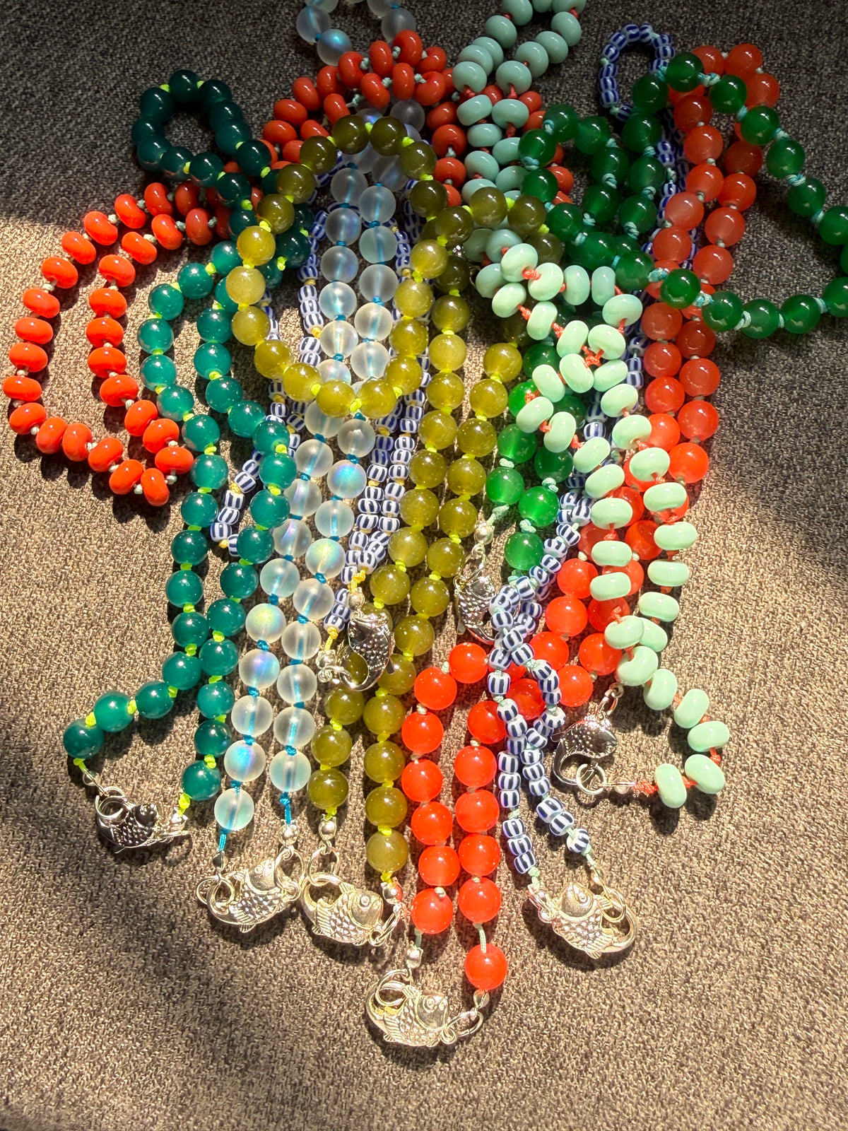 A pile of colorful beaded necklaces, each with a silver-toned fish clasp